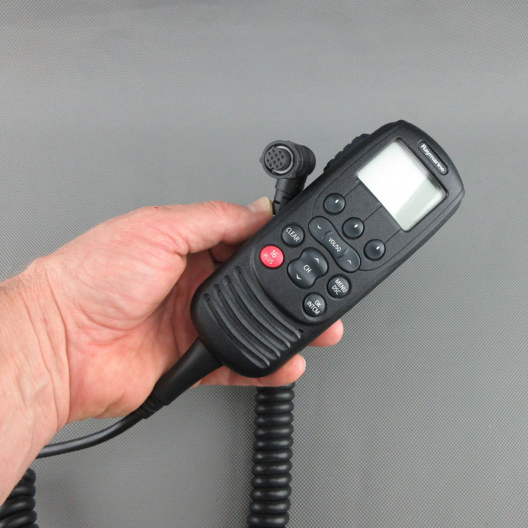 Vista frontal del auricular VHF Raymarine® Ray260 A80197 reacondicionado, sostenido en la mano, con el conector visible.