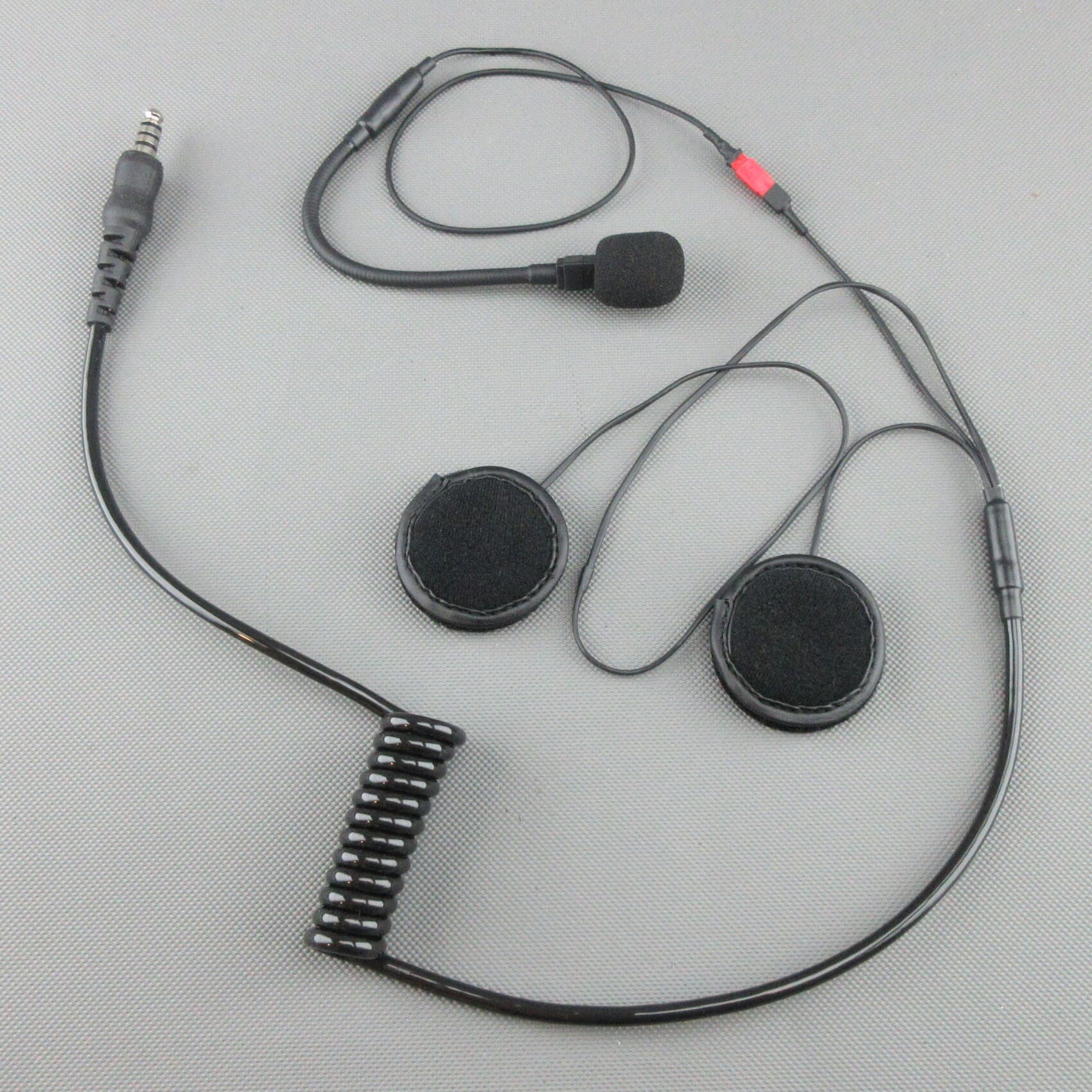 Se muestra un kit de instalación de casco de competición para cascos abiertos con altavoces, un micrófono de cuello de cisne, un cable de conexión espiralado y un conector jack TP-120 con compatibilidad Peltor®.