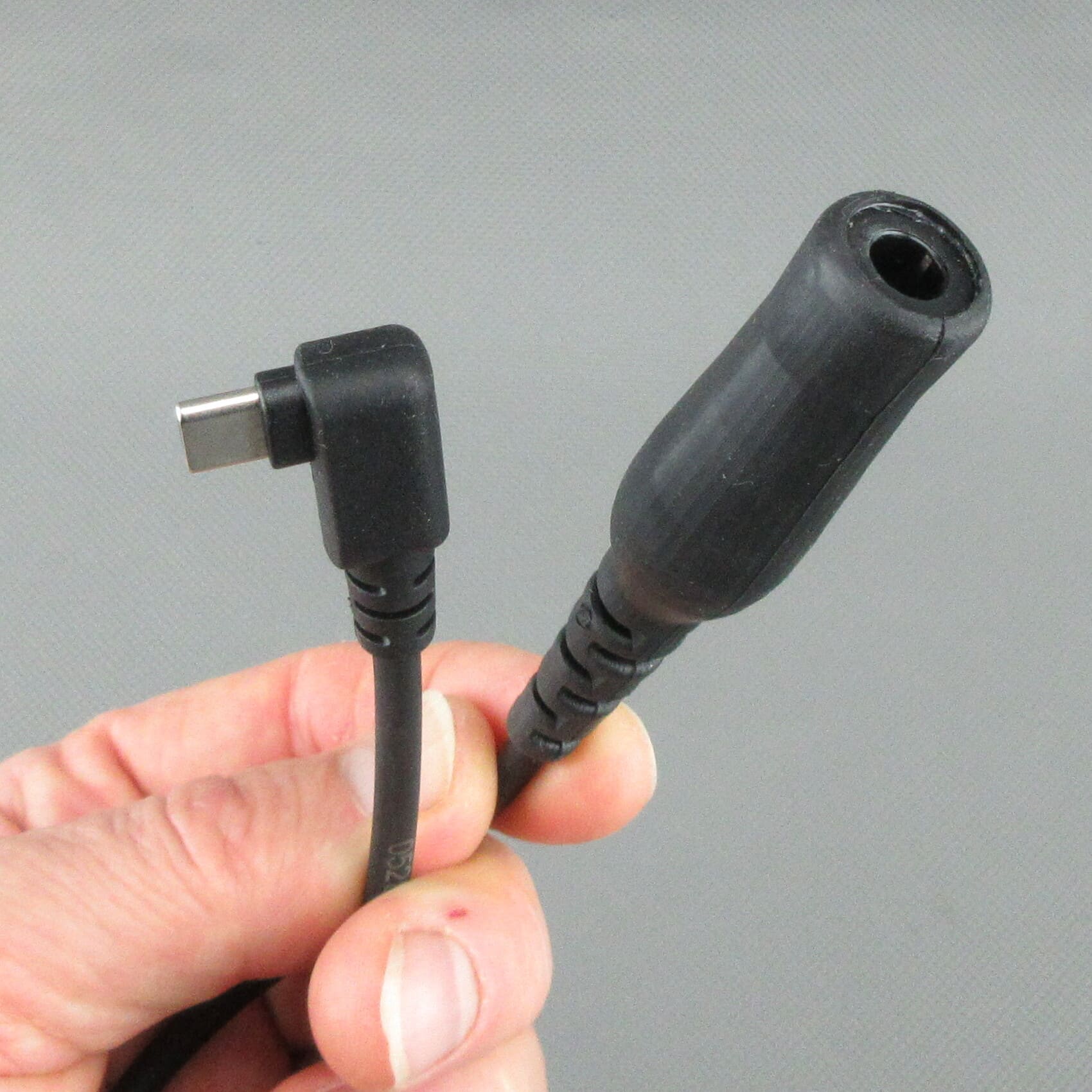 Mano sujetando el cable adaptador StarCom1 FLX2, con el foco en el conector USB-C acodado y el conector hembra TP-120 (compatible con Nexus® / Amphenol®) para conectar cascos tácticos con cableado NATO.