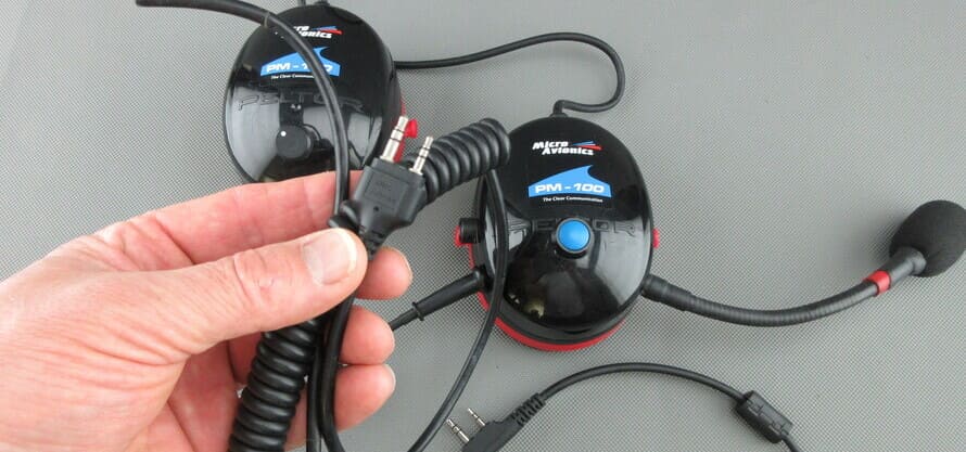 Auriculares MicroAvionics® con cable de conexión para radio, mostrando el conector de radio sostenido en una mano.